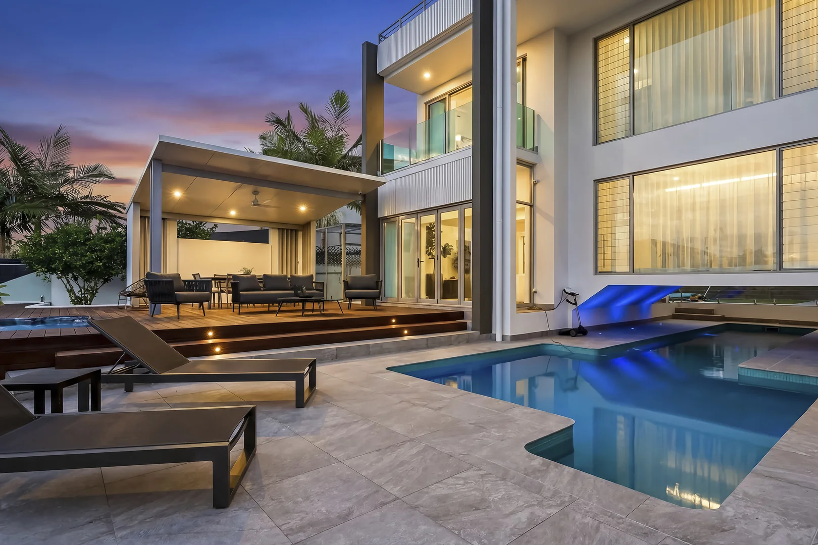 Covered outdoor gazebo at dusk with recessed downlights, outdoor lounge and dining furniture beside the pool.