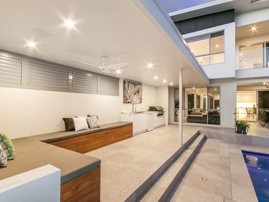 Covered poolside cabana with built-in seating, an outdoor kitchen and ceiling fans beside the main house.