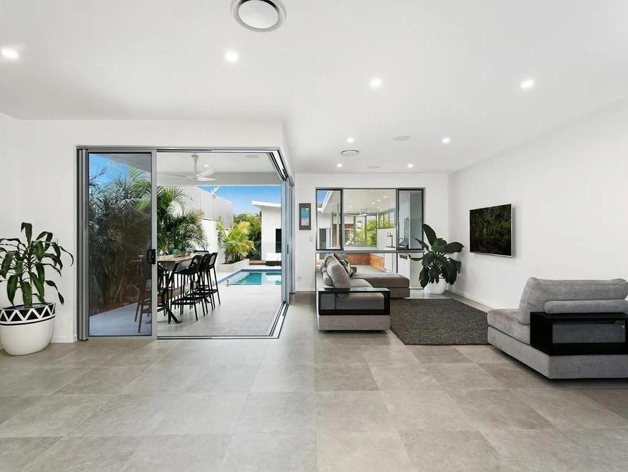 Living room with grey sofas and a wall-mounted television, opening to outdoor dining and the pool.