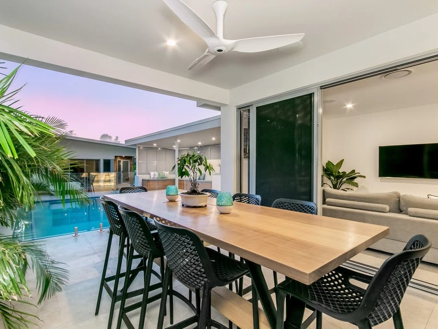 Covered outdoor dining table beside the pool, with the living-room television visible through open doors.