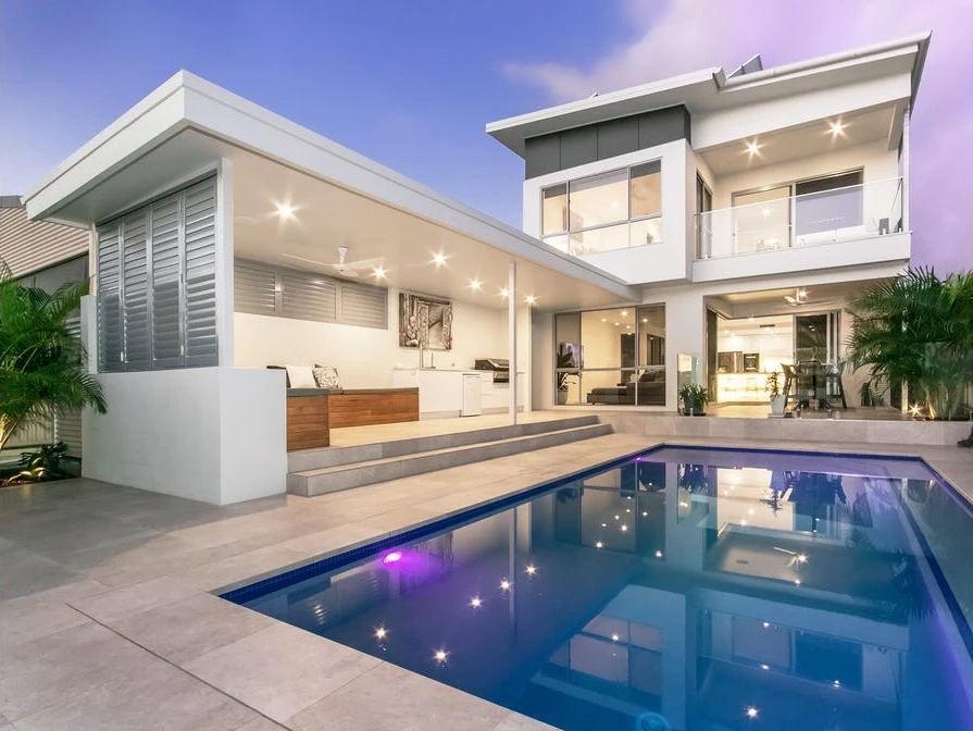 Two-storey Cypress Terrace home and covered cabana overlooking the illuminated pool at dusk.