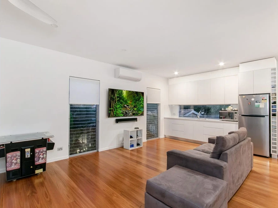 Living space with a kitchenette, grey sofa, wall-mounted television and soundbar.