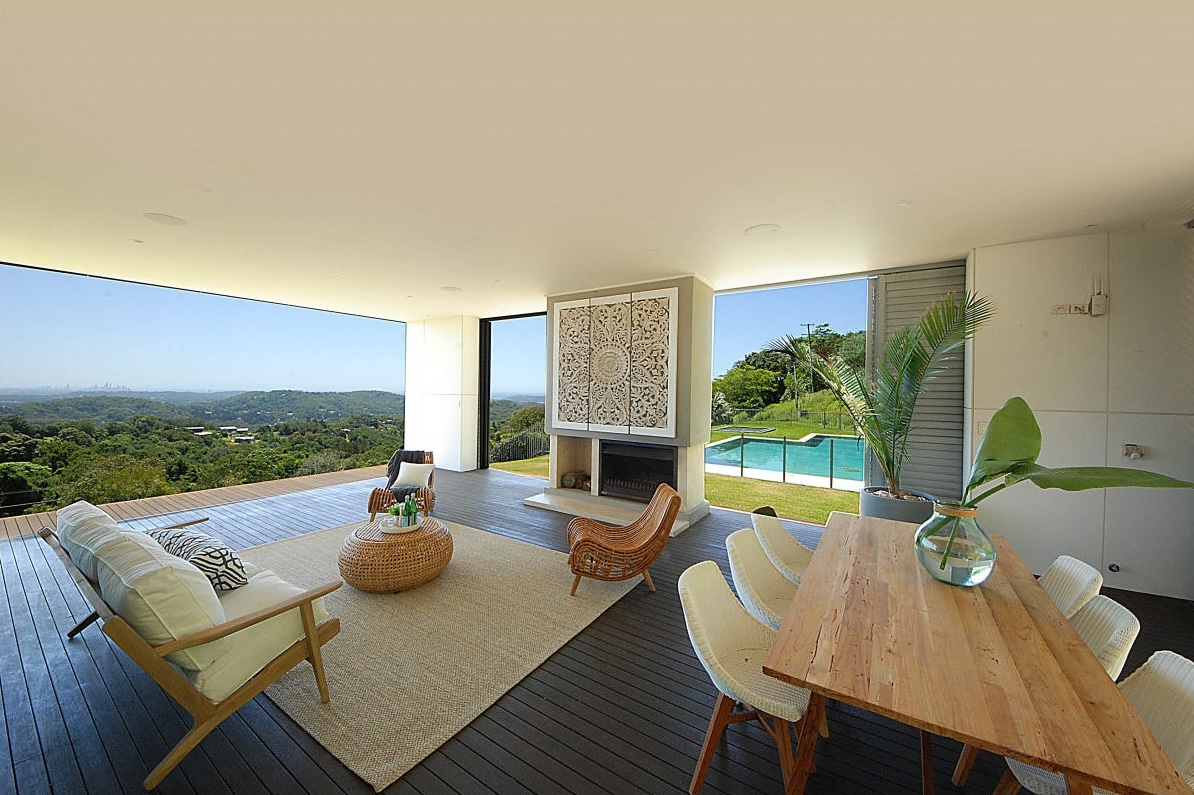 Covered outdoor terrace at Brocks Road with a sofa, rattan chairs and a timber dining table, opening to wide hinterland views.