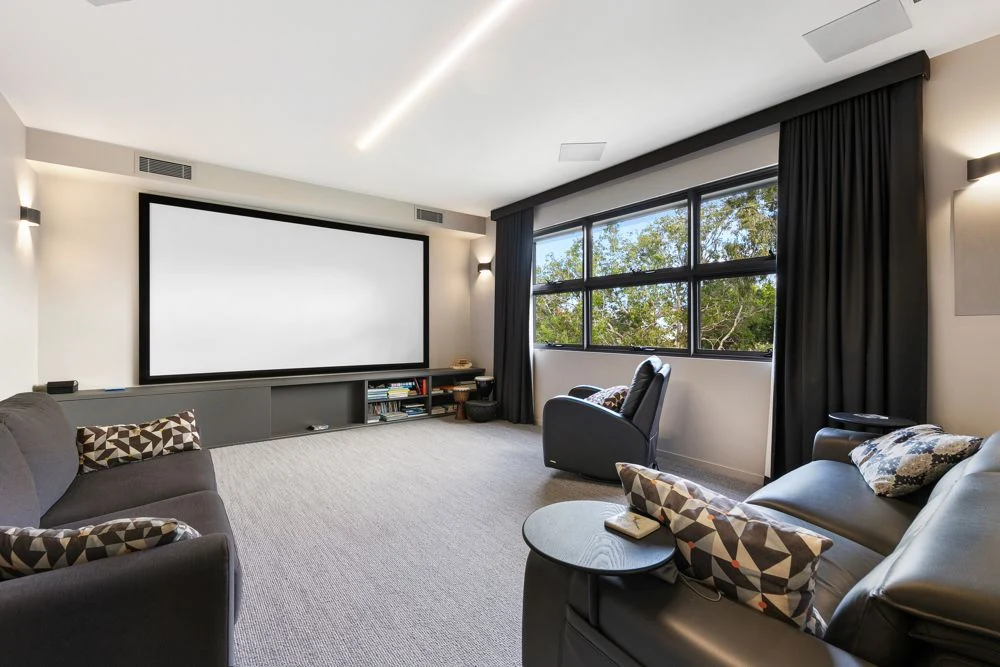 Home cinema with a large projection screen, lounge seating, ceiling speakers and dark curtains.