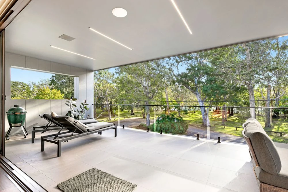 Covered deck with lounge chairs, a glass balustrade and views into trees.