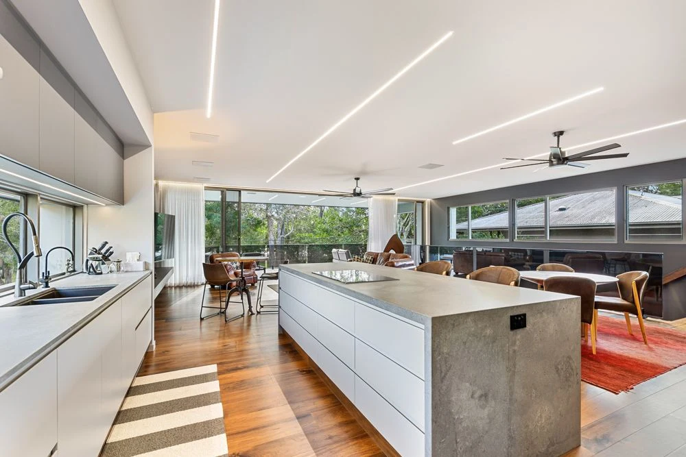 Kitchen island beneath linear ceiling lights, with dining and living spaces beyond.