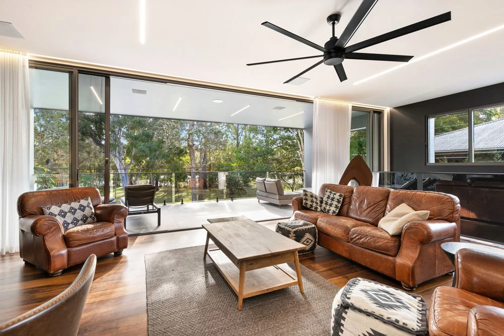 Living room at Michel Drive with leather seating, linear ceiling lighting and large doors opening towards a deck.
